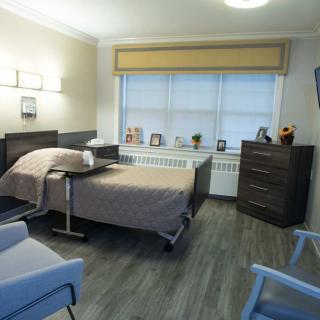 A clean and organized hospital room with a bed, bedside table, and comfortable seating.