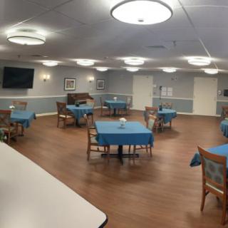 A spacious dining area with neatly arranged tables and chairs, featuring soft lighting and a television on the wall.