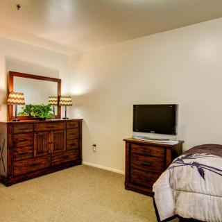 A cozy bedroom featuring a dresser with a mirror, lamps, and a small television on a side table.