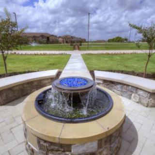 A beautifully designed outdoor fountain with a stone base, set in a landscaped garden with a pathway leading into the distance.