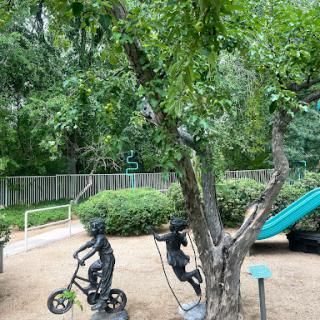 A vibrant playground scene featuring trees, a swing, a slide, and playful statues.