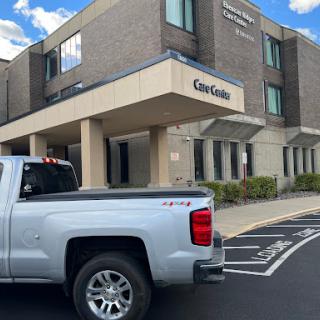 A pickup truck parked in front of a healthcare facility under a partly cloudy sky.