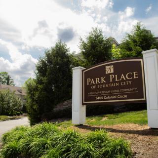 Entrance sign for Park Place apartment complex surrounded by trees and a cloudy sky.