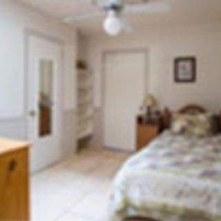 A cozy bedroom with a neatly made bed, a mirror on the door, and shelves for storage.