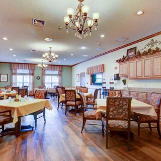 A spacious dining room with elegant chandeliers, neatly arranged tables and chairs, and a warm, inviting ambiance.