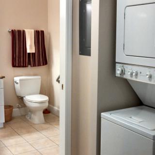 A compact dual-purpose room featuring a bathroom with a toilet and towels, alongside a laundry area with a stacked washer and dryer.