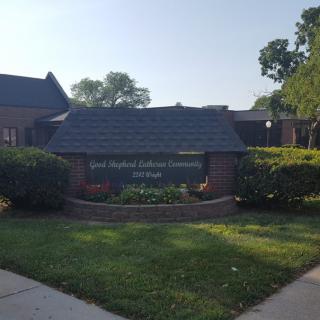 A building entrance with a sign surrounded by well-maintained greenery and trees.