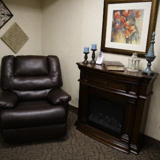 A cozy corner featuring a brown leather recliner next to an elegant wooden fireplace and decorative artwork.