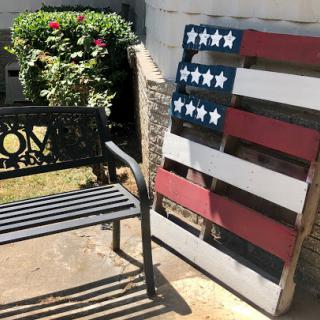 A creatively designed flag made from wooden pallets beside a bench in an outdoor setting.