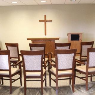 A small chapel with rows of chairs facing an altar and a cross on the wall.