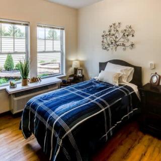 A cozy bedroom with a single bed featuring a plaid blanket and natural light flowing in through the windows.