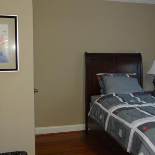 A bedroom with a neatly made bed, bedside lamp, and framed picture on the wall.