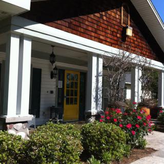 A charming house featuring a vibrant yellow door and beautifully landscaped flowers.