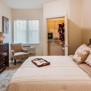 A cozy bedroom with a neatly made bed, a chair by the window, and a dresser.