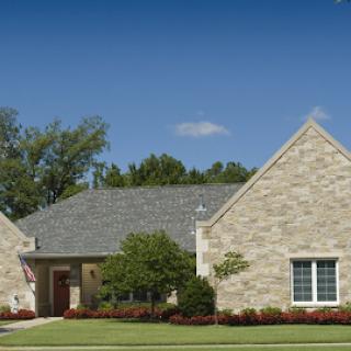 A beautiful single-story house with a stone exterior, surrounded by lush landscaping under a clear blue sky.