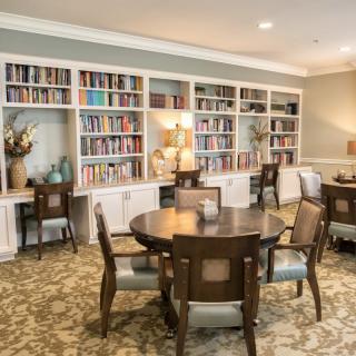 A cozy library room with bookshelves and a reading area featuring tables and chairs.
