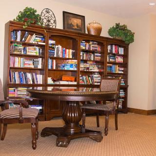 A cozy home office featuring a wooden bookshelf filled with books, a round table, and comfortable chairs.