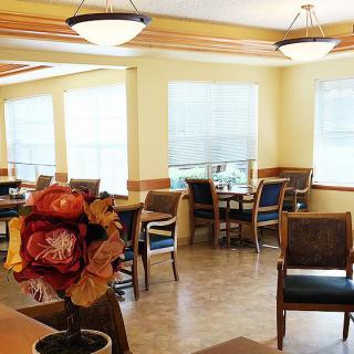 A well-lit dining area with several tables and chairs, featuring large windows and decorative lighting.