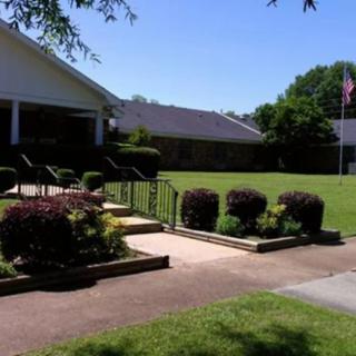 A sunny outdoor scene with a building, neatly trimmed bushes, and a wide lawn.