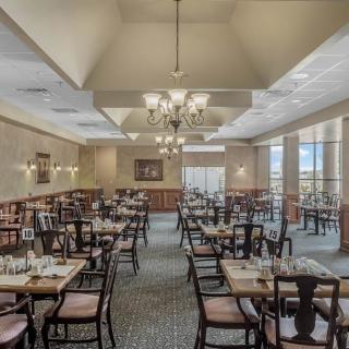 An elegant dining space with arranged tables and chairs, showcasing chandeliers and large windows for natural light.