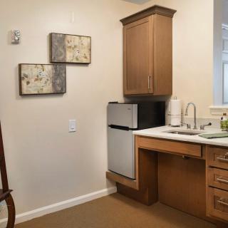 A compact kitchenette with a small fridge, wooden cabinets, and decorative wall art.
