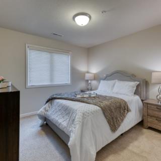 A cozy bedroom with a neatly made bed, bedside lamps, and a window providing natural light.