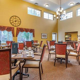 A well-lit dining area with neatly arranged tables and chairs, featuring elegant decor and a high ceiling.