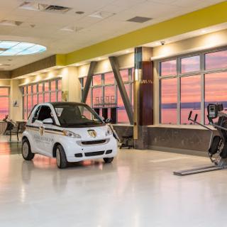A unique gym interior featuring a compact car alongside fitness equipment, bathed in the warm glow of a sunset.
