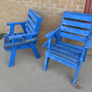 Two blue wooden chairs placed against a brick wall.