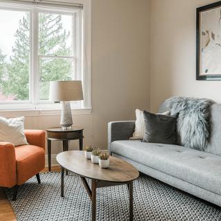 A cozy living room with a gray sofa, orange armchair, and a wooden coffee table under a bright window.