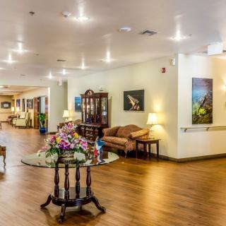 A well-lit lobby area featuring a central table with floral decorations, surrounded by comfortable seating and artwork on the walls.