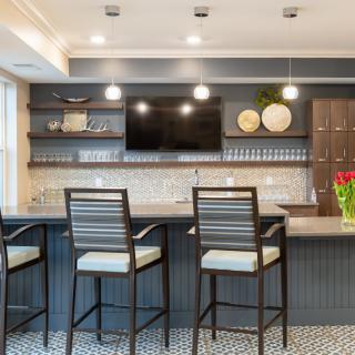 A modern home bar area with stylish bar stools, a large countertop, and decorative shelving.