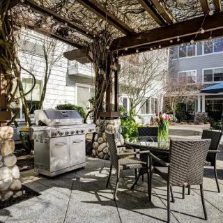A cozy outdoor patio with a pergola, seating area, and grill in a residential setting.