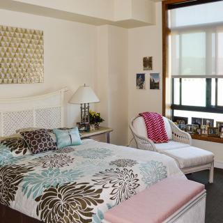 Cozy bedroom with floral bedding, a comfortable chair, and natural light from the window.