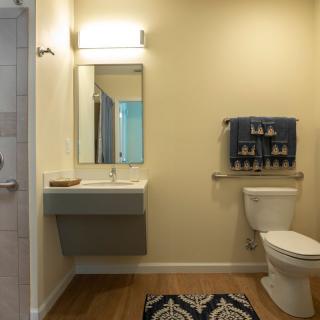 A modern bathroom with a wall-mounted sink, mirror, and toilet next to a towel rack.