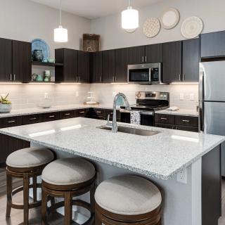 A modern kitchen featuring an island with granite countertops, stainless steel appliances, and dark cabinetry.