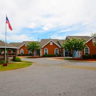 A complex of red brick buildings with an American flag flying in the front, surrounded by trees and a paved driveway.
