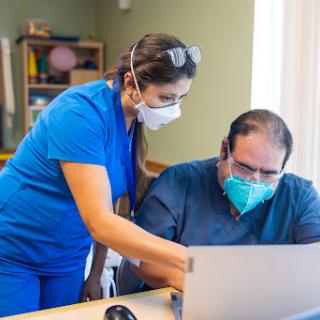 A healthcare professional assists a patient with using a laptop in a medical setting.