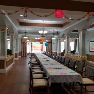 A decorated dining room prepared for a festive event, featuring a long table with chairs and colorful balloons and garlands.