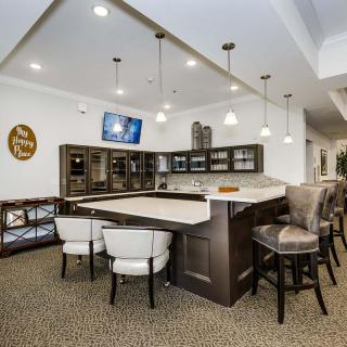 A modern kitchen interior featuring a countertop with bar stools, pendant lighting, and a wall-mounted television.