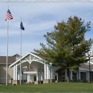 A building with an American flag and another flag on tall poles in front, surrounded by trees under a clear sky.