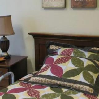 A cozy bedroom scene featuring a quilted bed and a lamp on the nightstand.