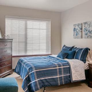 A cozy bedroom featuring a bed with blue plaid bedding, a wooden dresser, and a window with blinds.