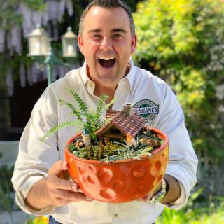 A cheerful person holding a decorative bowl with plants in an outdoor setting.