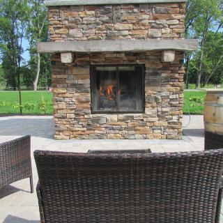A cozy outdoor patio featuring a stone fireplace surrounded by wicker chairs.