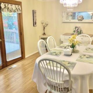A cozy dining room with a round table, surrounded by white chairs and adorned with fresh flowers under a chandelier.