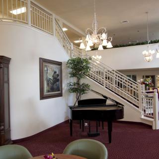 A spacious interior featuring a grand piano and elegant staircase under ornate chandeliers.