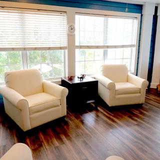 A cozy living room area with two cream-colored armchairs, a small table in between, and large windows letting in natural light.