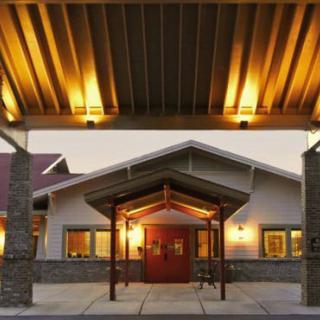 Illuminated entrance of a building with a peaked roof and columns during the evening.