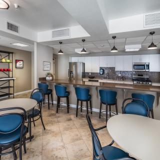 A modern kitchen and dining area with barstools and tables, featuring contemporary lighting and decor.